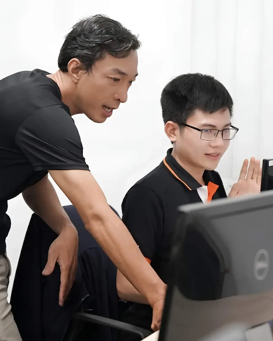 A senior InApps engineer leaning in to point at a screen beside a younger colleague in the Ho Chi Minh City office